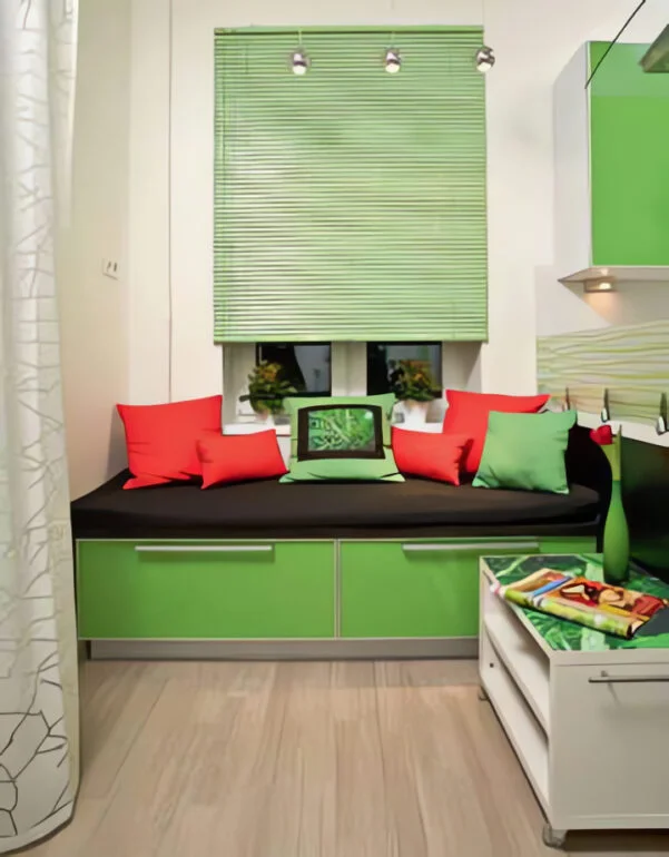 У кушетки, установленной под окном, нет спинки, но её заменяют декоративные подушки красного, чёрного и светло-зелёного цвета